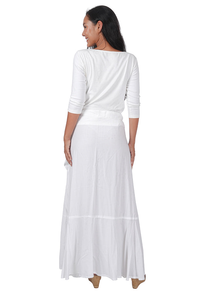 Back view of a woman wearing a white top with an ankle length, side-tied, flowing white skirt on a white background.