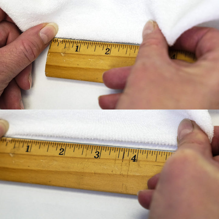 Hands measuring white terry cloth fabric's stertch properties with a wooden imperial system ruler on a white background.