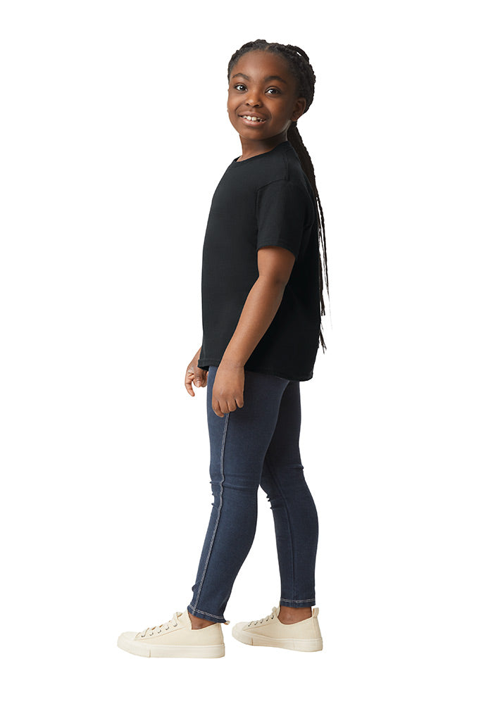 Side view of a young girl wearing a Gildan 5.3 oz. heavy cotton, short-sleeved black t-shirt and blue jeans on a white background.