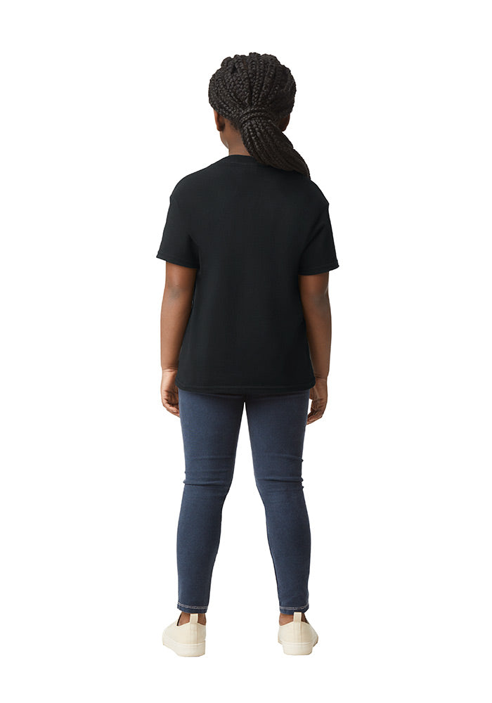 Back view of a young girl wearing a Gildan 5.3 oz. heavy cotton, short-sleeved black t-shirt and blue jeans on a white background.